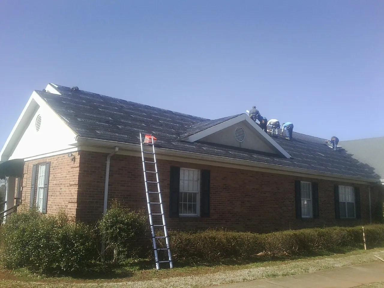 Crew tearing shingles off a brick ranch roof with a ladder set — Emergency Roof Repair work by our crew in Deer Creek