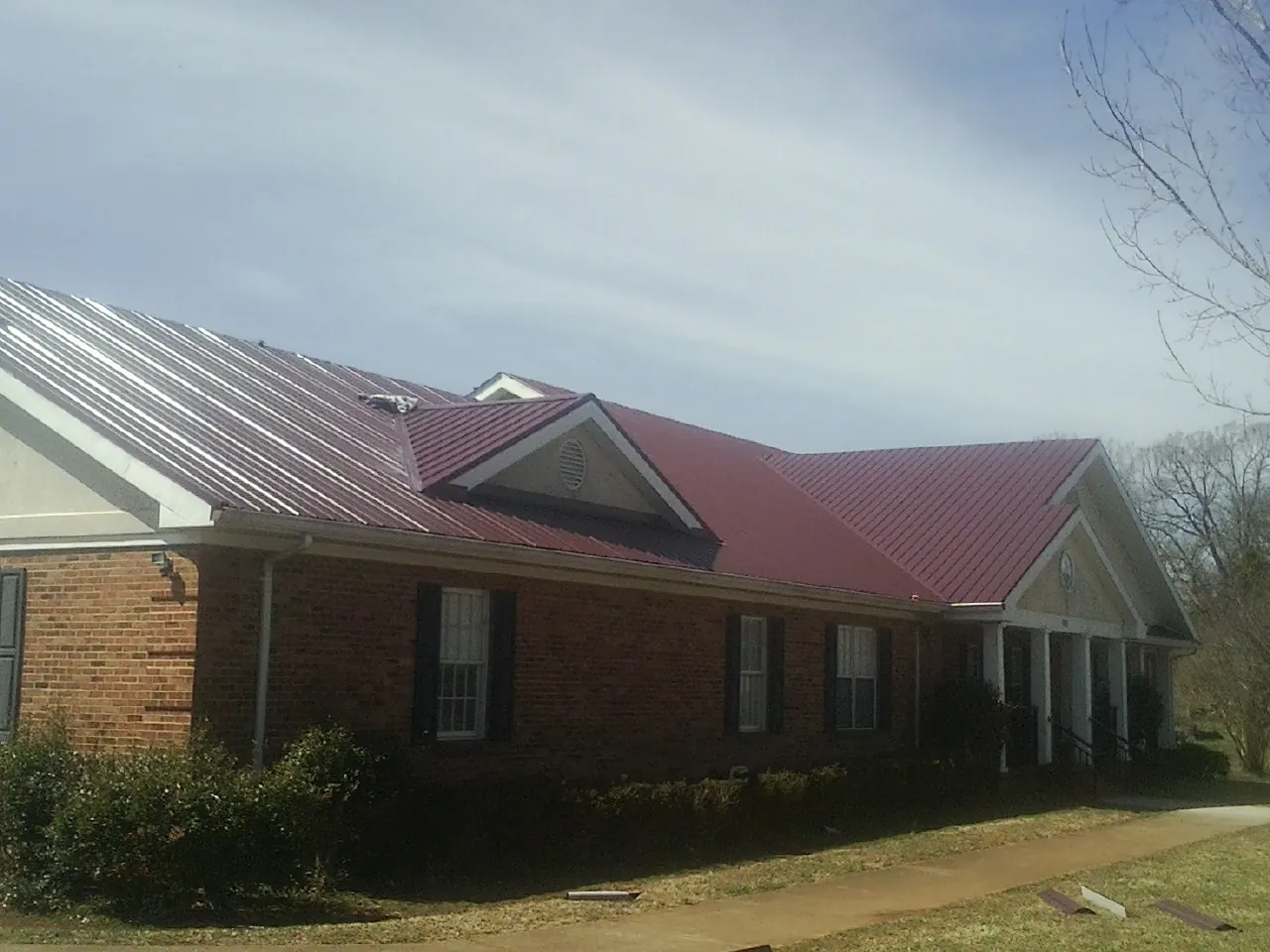 Red metal roof with gabled entries on a long brick building, from a Hail Damage Roof Repair job in Deer Creek