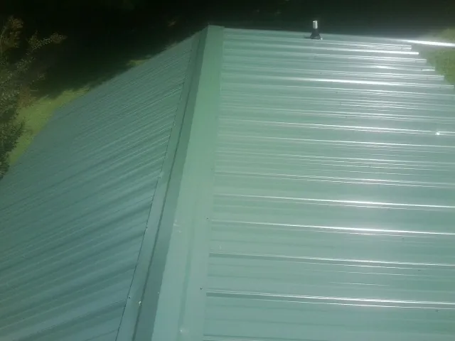 New green metal panels meeting at the ridge of a roof — Flat Roof Repair work by our crew in Deer Creek
